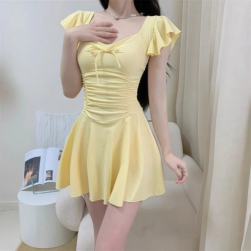 Woman wearing a pale yellow ruffled one-piece swimsuit with a bow detail.