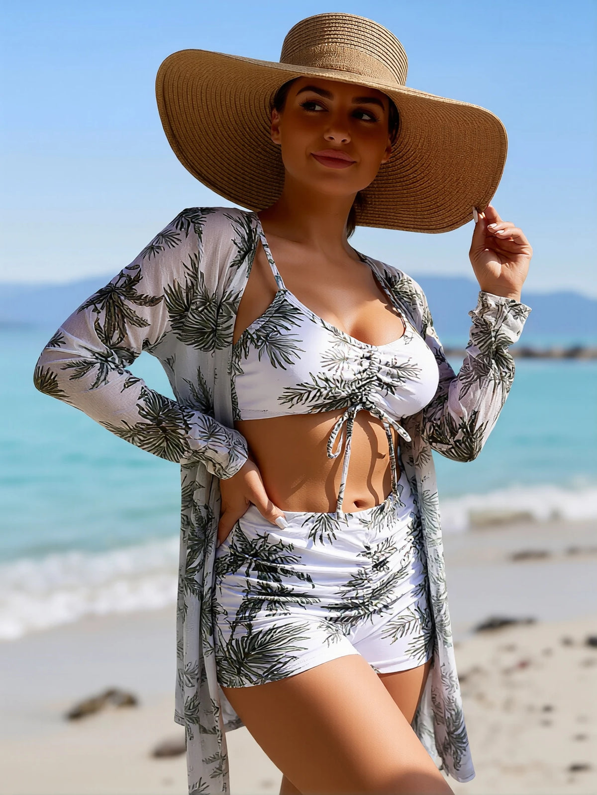Woman wearing a white tropical palm print bikini set with matching cover-up and straw hat on a beach