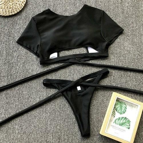Two-piece black bikini set with crop top and tie-side bottoms on a gray background.