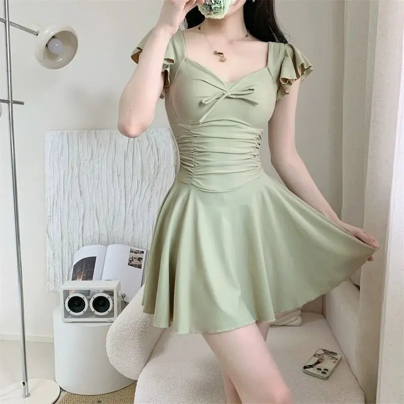 Sage green one-piece swimsuit with ruffled sleeves and a flared skirt design.