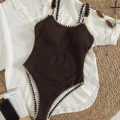 Dark brown textured crochet one-piece swimsuit with cream scalloped edges on a white shirt.