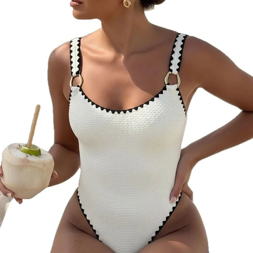 Woman wearing a white textured one-piece swimsuit with black trim and gold ring details.