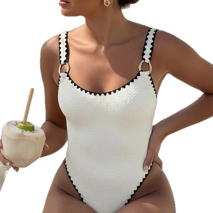 Woman wearing a white textured one-piece swimsuit with black trim and gold ring details.