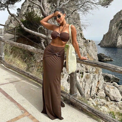 Woman in a brown two-piece bikini set and matching maxi skirt posing by a coastal cliff.