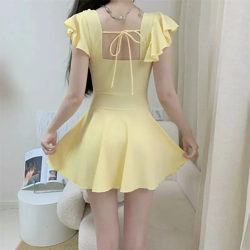 Woman wearing a pale yellow ruffled one-piece swimsuit with a tie-back design.