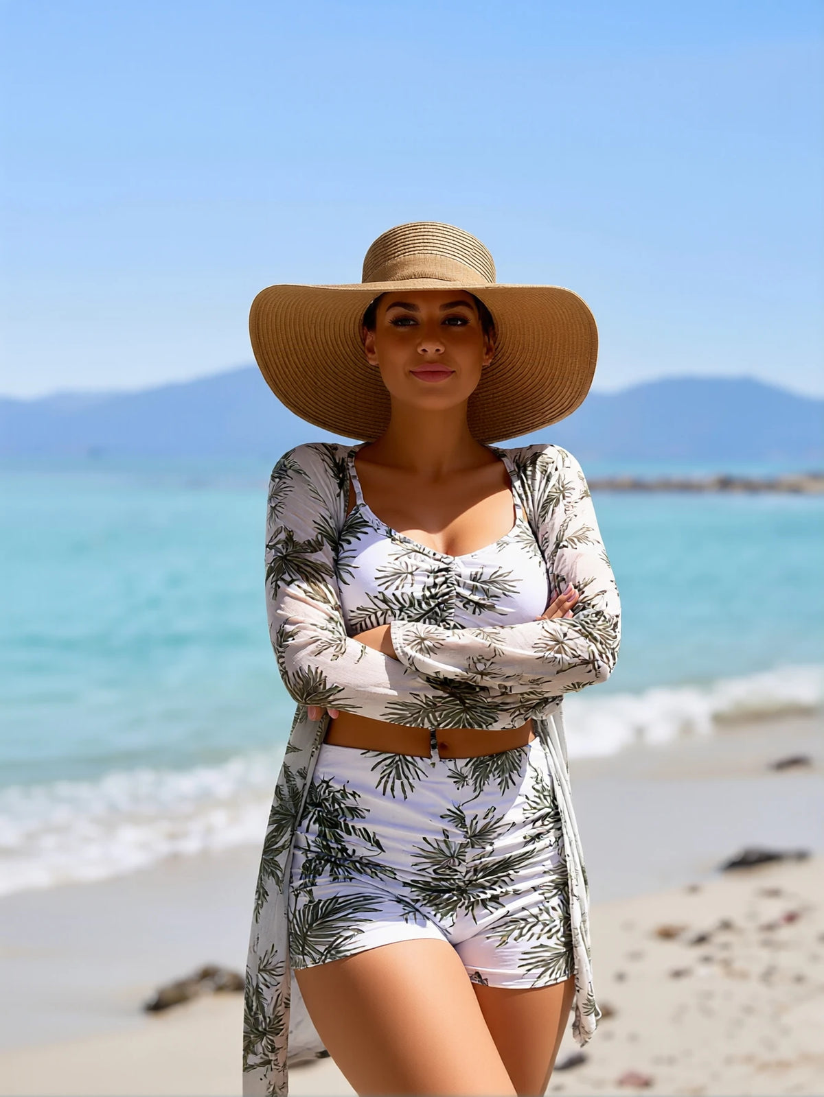 Woman in a tropical print bikini set, matching cover-up, and sun hat on a sandy beach.
