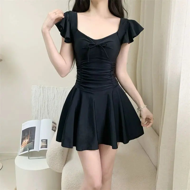 Woman wearing a black one-piece swimsuit with ruffle sleeves and a flared skirt design.