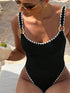 Woman in a black crochet one-piece swimsuit with white scalloped edges and gold ring details.