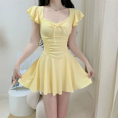 Woman wearing a pale yellow ruffled one-piece swimsuit with a bow detail and flared skirt.