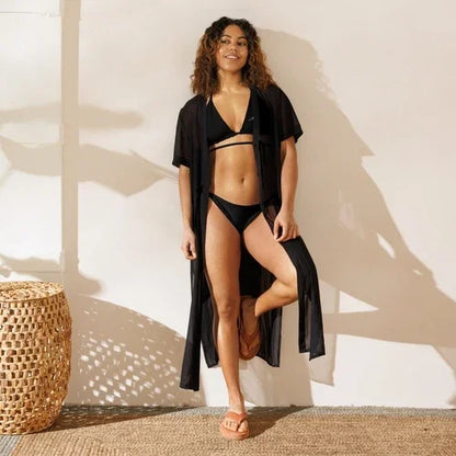 Woman wearing a black bikini set and a long black sheer beach cover-up