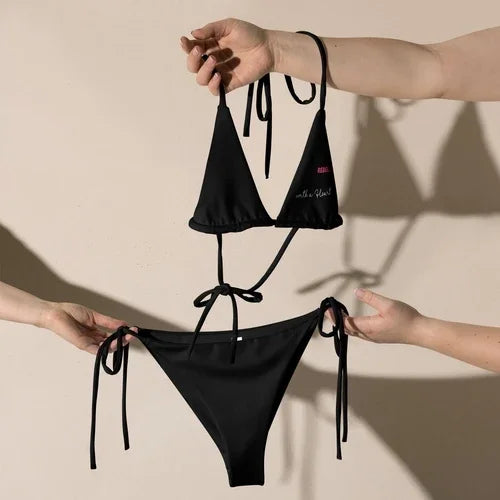 Two pairs of hands holding up a black string bikini set against a neutral background.