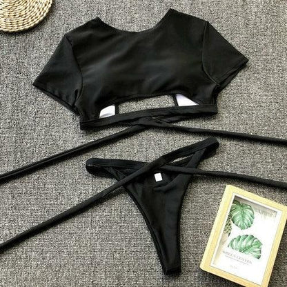 Two-piece black wrap-around bikini set with a crop top and matching bottoms on a grey surface.