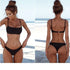 Woman wearing a minimalist black two-piece bikini set on a sunny beach.